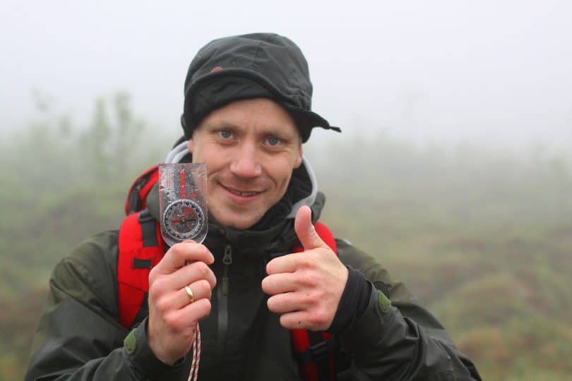 A guy holding a compass and showing thumbs up