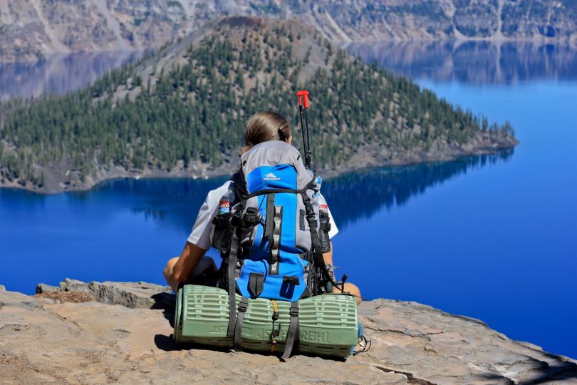 Girl backpacker is sitting on rock peak over lake