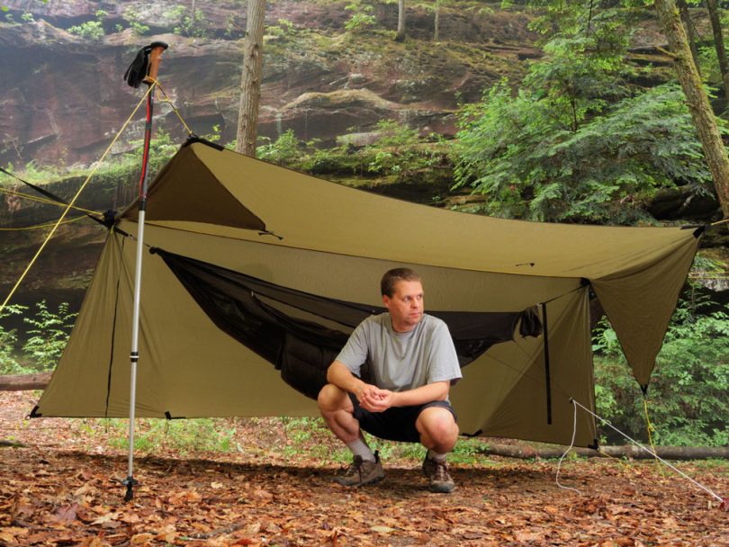 Man near modern camping hammock under tarp