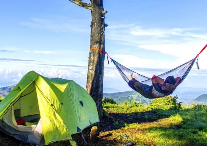 Man lying hammock beside camping tent