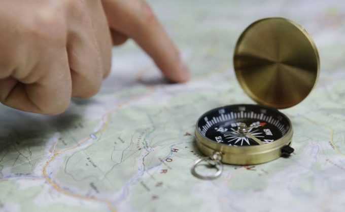 Men's finger planning hiking trip on a map with compass